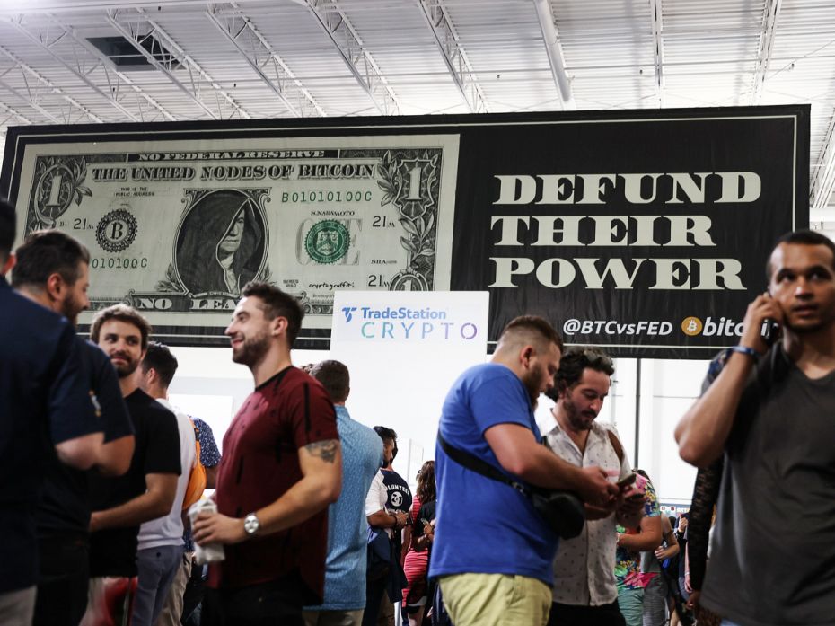 A mocking bill note declaring ‘No federal reserve here’ hangs above attendees taking a b