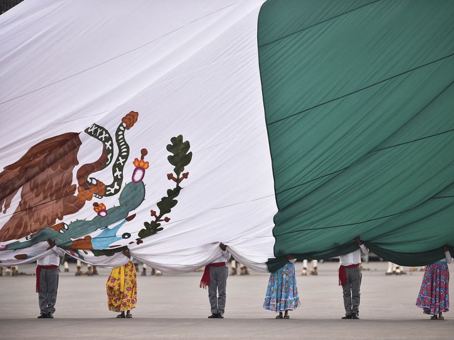Members of the Mexican army dressed as revolutionary soldiers hold the national flag while commemora