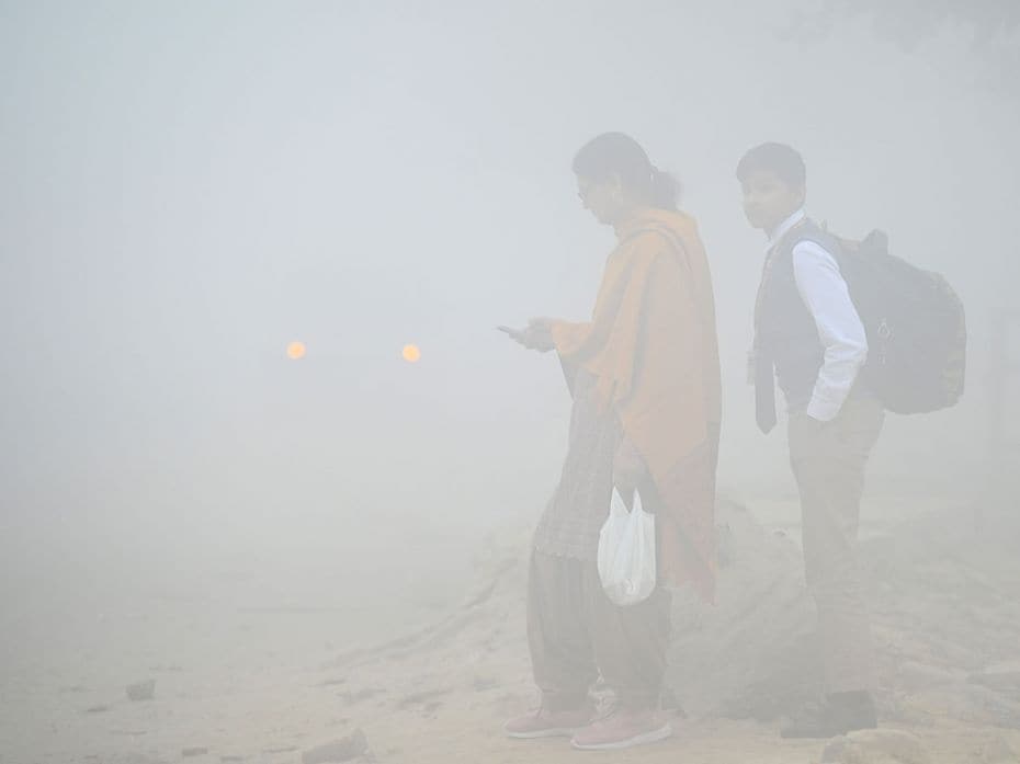 A woman waits for the school bus to pick up her son amidst heavy smog and reduced visibility in Noid