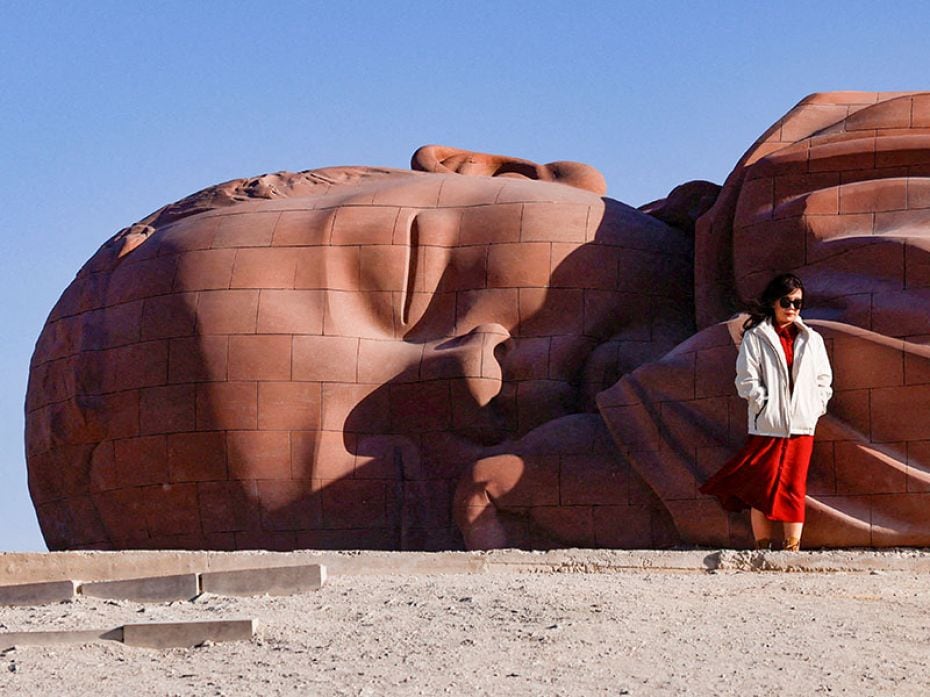 A tourist poses for pictures in front of a Buddhist sculpture in the Gobi desert in Guazhou, Gansu p