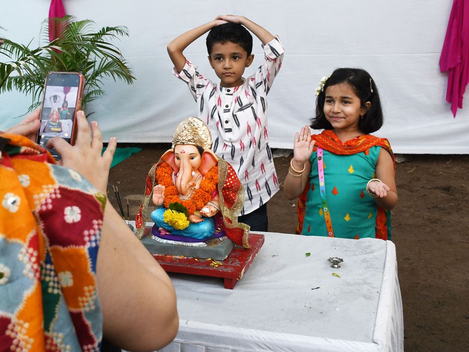 Posing for a photo with her brother, a girl assumes the posture of the Ganesh deity at a home in Mum