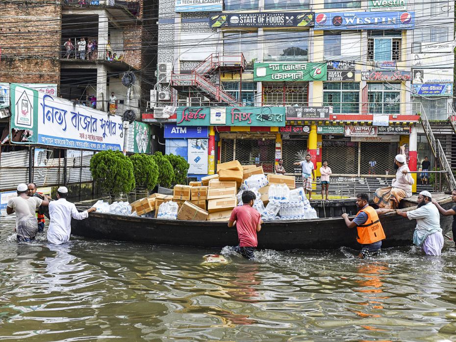 Volunteers wade through floodwaters and transport relief material on a boat for flood-affected peopl